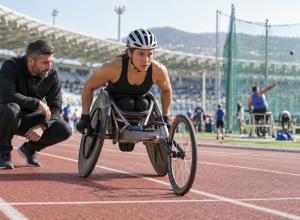 Para sportiste sacensību riteņkrēslā gatavojas startam kopā ar treneri stadionā