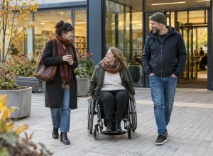 Sieviete riteņkrēslā sarunājas ar draugiem pie pieejamas kopienas ēkas