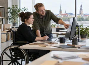 Sieviete riteņkrēslā kopā ar kolēģi apgūst uzdevumu pie piekļūstamas darba vietas