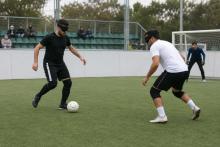 Divi spēlētāji ar acu aizsegiem sacenšas par bumbu neredzīgo futbola laukumā ar sānu apmalēm.