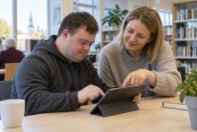 Vīrietis un pasniedzēja bibliotēkā kopīgi izmanto planšetdatoru
