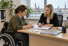 Sieviete riteņkrēslā kopā ar sociālo darbinieci pārskata čekus un pabalsta dokumentus