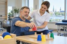 Pacients rehabilitācijas telpā vingrina rokas kustību fizioterapeites vadībā