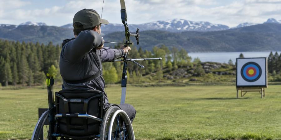 Para loka šāvējs sporta riteņkrēslā tēmē ar loku uz mērķi āra treniņu laukumā.