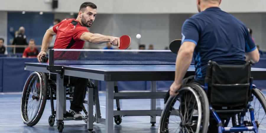 Divi para galda tenisisti riteņkrēslos izspēlē bumbiņu pie galda sporta hallē