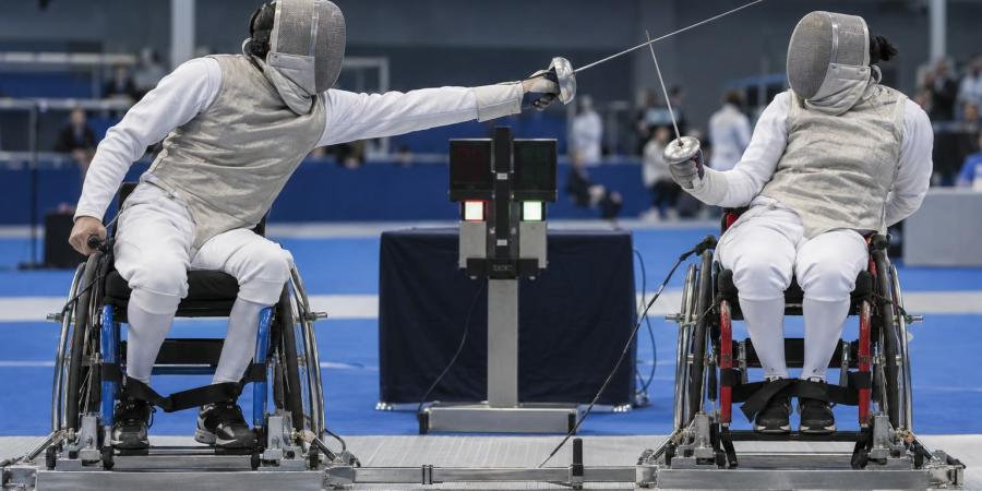 Divi para paukotāji nostiprinātos riteņkrēslos sacenšas uz metāla rāmja sporta hallē