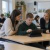 Skolēns klasē lieto planšetdatoru, kamēr skolotāja un atbalsta speciāliste palīdz izvēlēties mācību darbību.