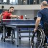Divi para galda tenisisti riteņkrēslos izspēlē bumbiņu pie galda sporta hallē