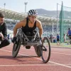 Para sportiste sacensību riteņkrēslā gatavojas startam kopā ar treneri stadionā