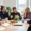 Cilvēki pie galda kopīgi apspriež psihiskās veselības pakalpojuma ieceri gaišā kopienas telpā