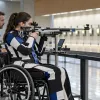Para šāvēja riteņkrēslā ar trenera atbalstu trenējas modernā iekštelpu šautuvē