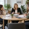 Mediatore vada sarunu pie apaļa galda ar diviem cilvēkiem, no kuriem viens izmanto riteņkrēslu
