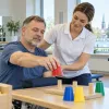 Pacients rehabilitācijas telpā vingrina rokas kustību fizioterapeites vadībā