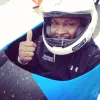 Sportists ķiverē bobslejā rāda paceltu īkšķi